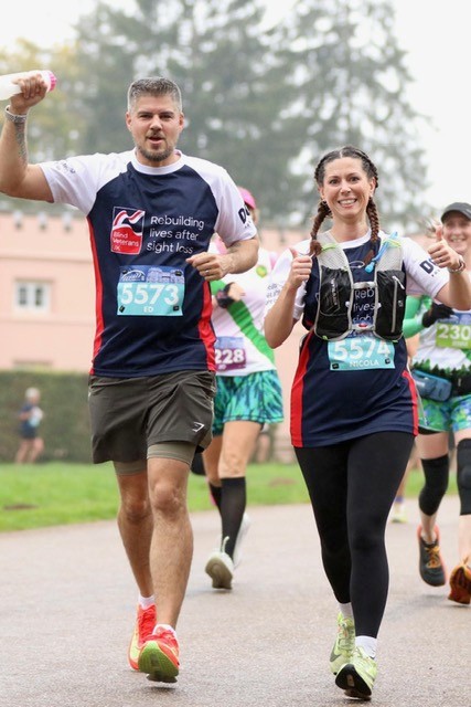 An action photo of Ed and Nicola during a race. They are wearing their Blind Veteran UK t-shirts and holding their thumbs up