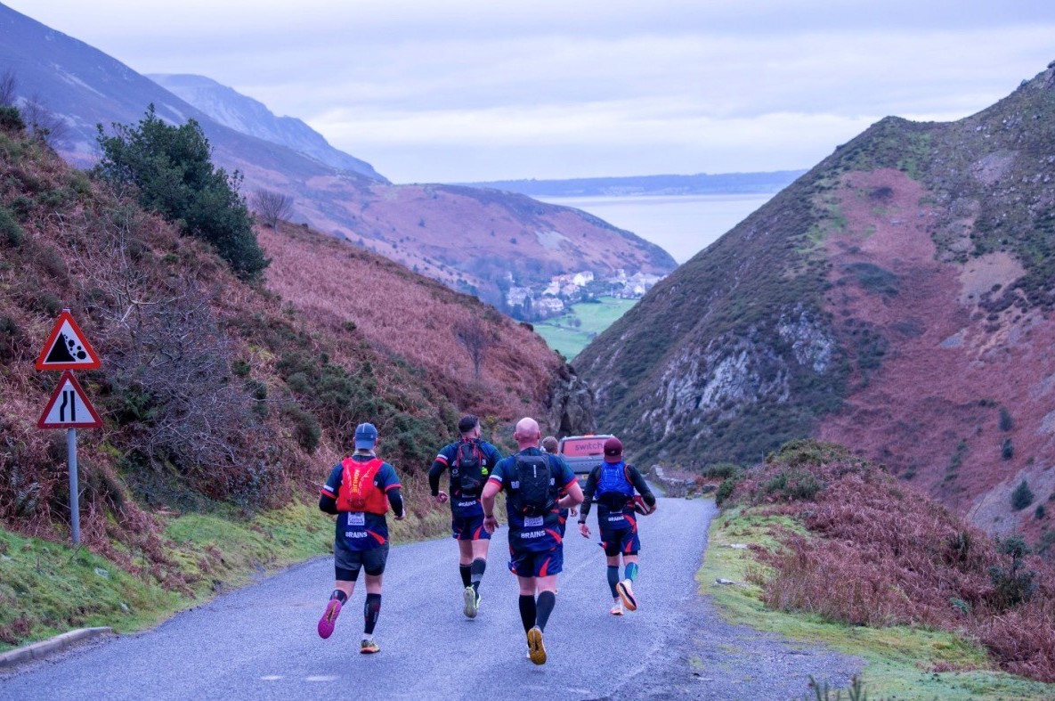 The team running down hill, away from the camera, on a road passing through hills with more hills in the distance.