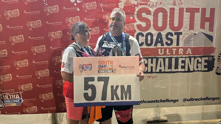 Andy and Angie holding a banner saying 57km with a large backdrop saying 'Finisher'