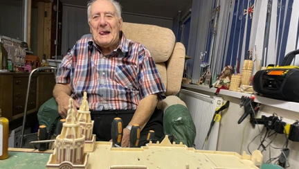 Maurice is smiling and sitting in front of a large model of a cathedral