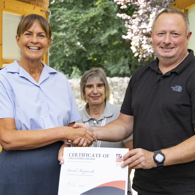 David shakes hands with WO Tracey Kenworthy as she delivers his certificate. Community Supporter Worker Chris stands in between them. They are all smiling.