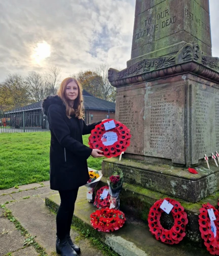 Stephanie stands next to the war memorial with wreaths already laid holding the wreath she is going to place