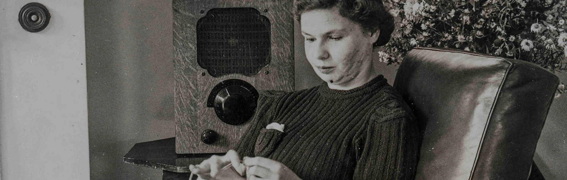 An archive photograph of a young blind veteran Barbara sitting on an armchair and sewing