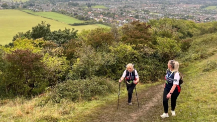 Jill and Ellie climbing up hill on a muddy pathway. Jill is using hiking sticks