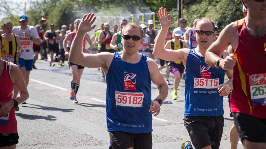 Photo of blind veteran Alan Lock, right and guide Dan, left, running past wearing Blind Veterans UK vest and waving at the camera