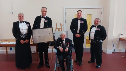 George is sat between four members of the HMS Sultan Mess. The Commanding Officer holds the photograph gifted to them by George.