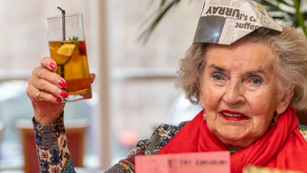 A blind veteran wearing a party hat, holding up a beverage and smiling