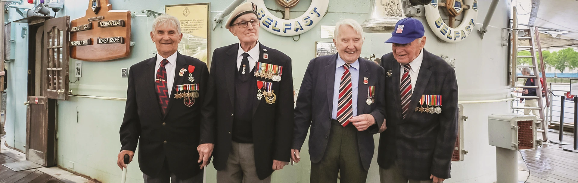 Four blind veterans, wearing their military badges and standing together, smiling and laughing