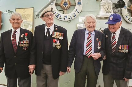 Four blind veterans, wearing their military badges and standing together, smiling and laughing