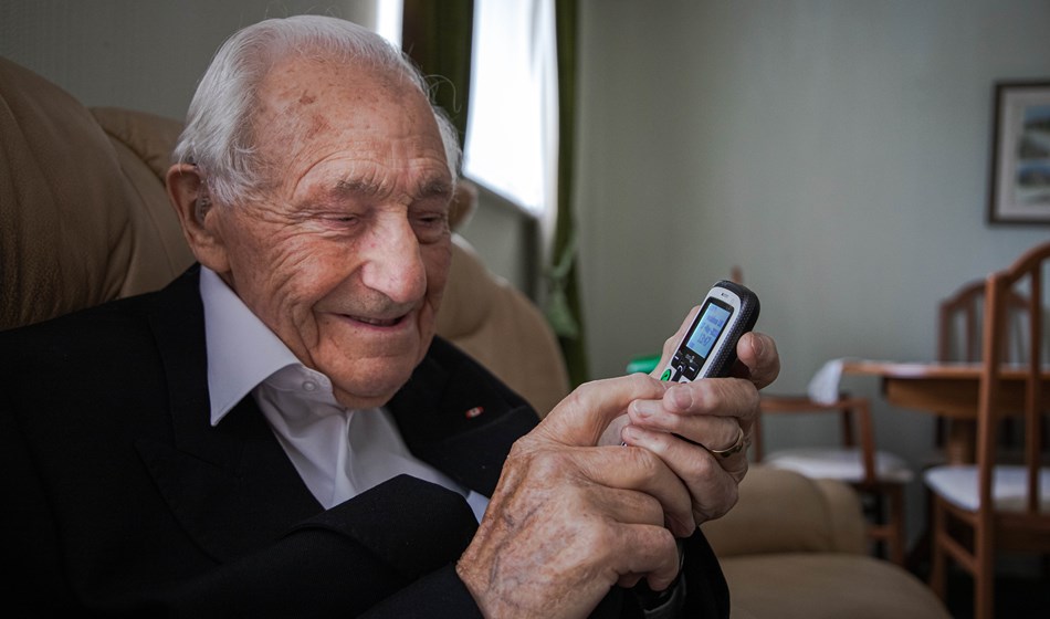 Blind veteran Ron in his living room, smiling as he holds a phone
