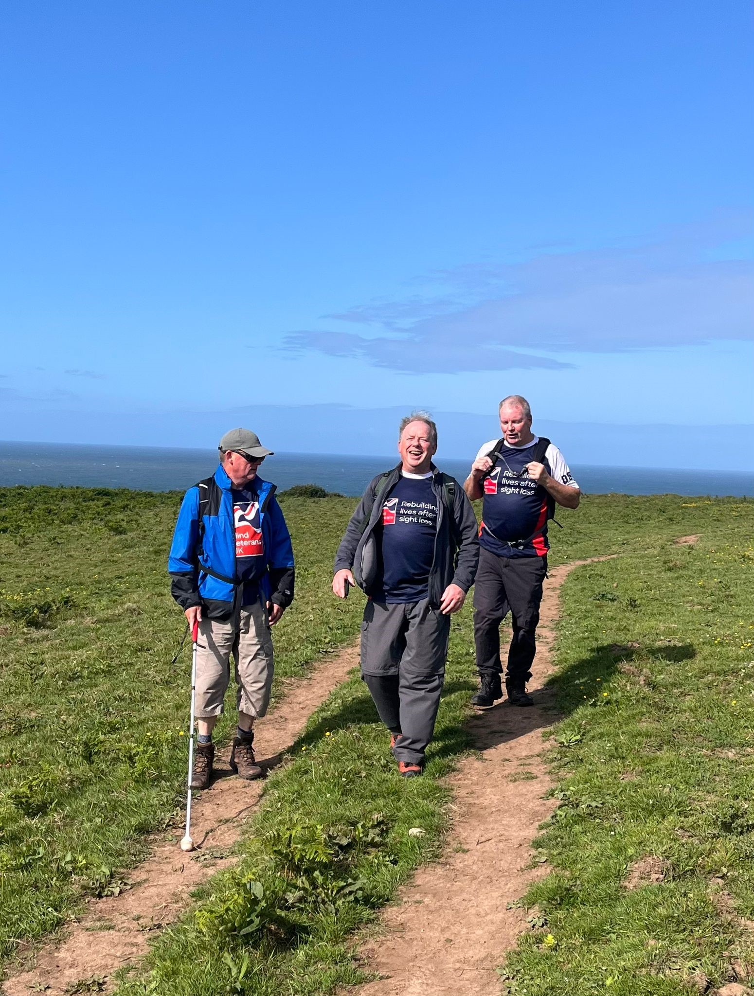 The three men all wearing Blind Veterans UK T-shirts make their way along tyre tracks with Phil slightly ahead with his white cane