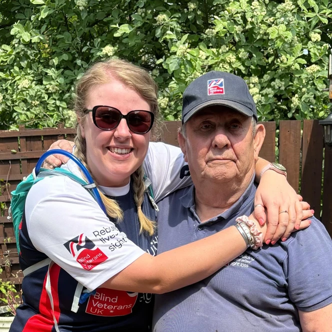 Rebecca wearing her Blind Veterans UK top with her arms around the neck of her Granda Brian.