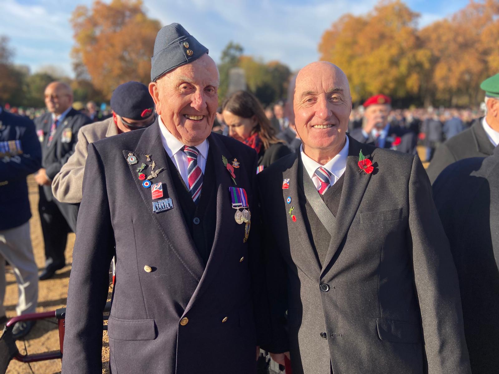 Michael and Eddie smile and look into camera. Both in smart suits, Michael also wears his medals and beret.