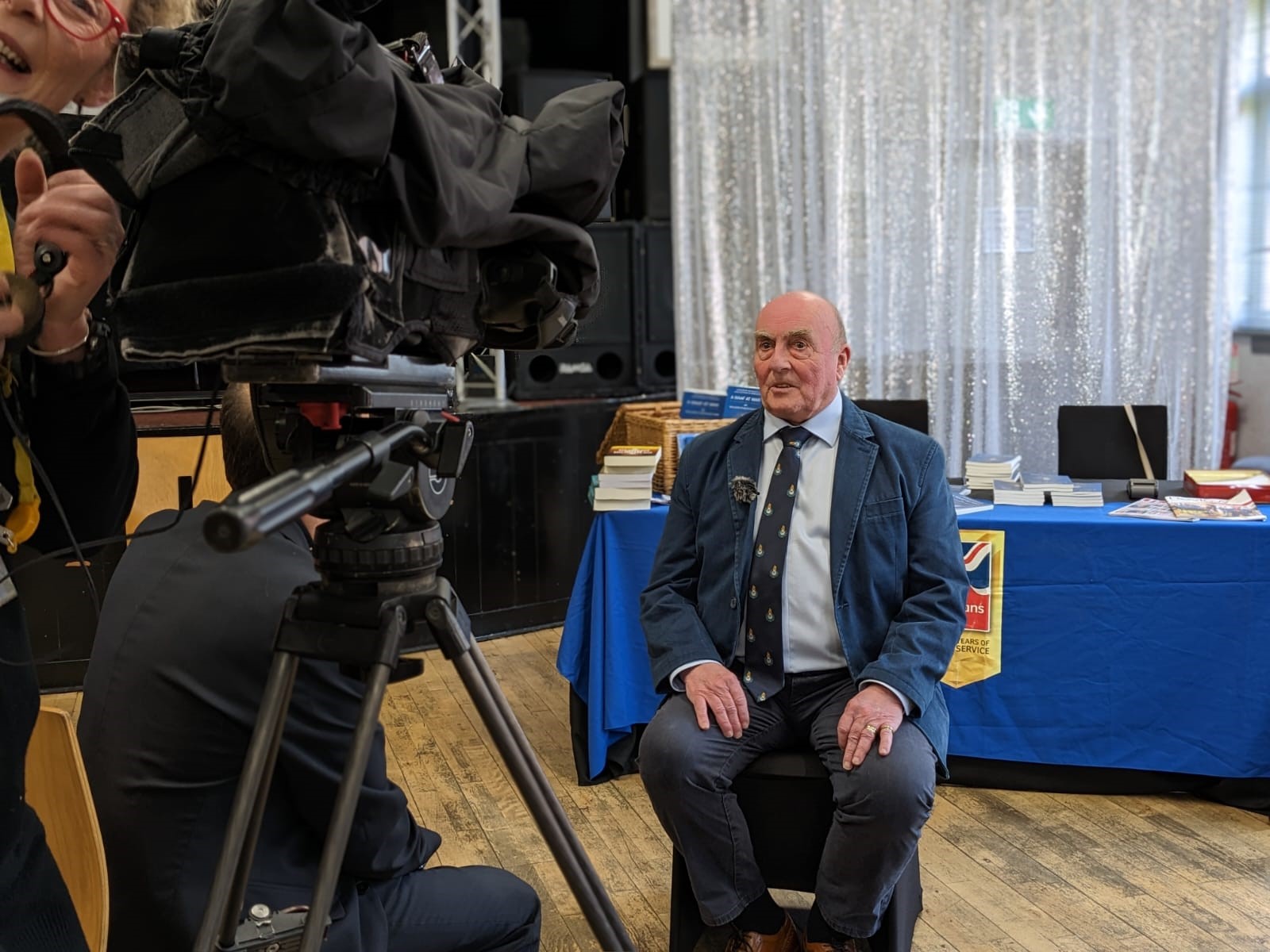 Simon is wearing a jacket and tie and looks into the camera