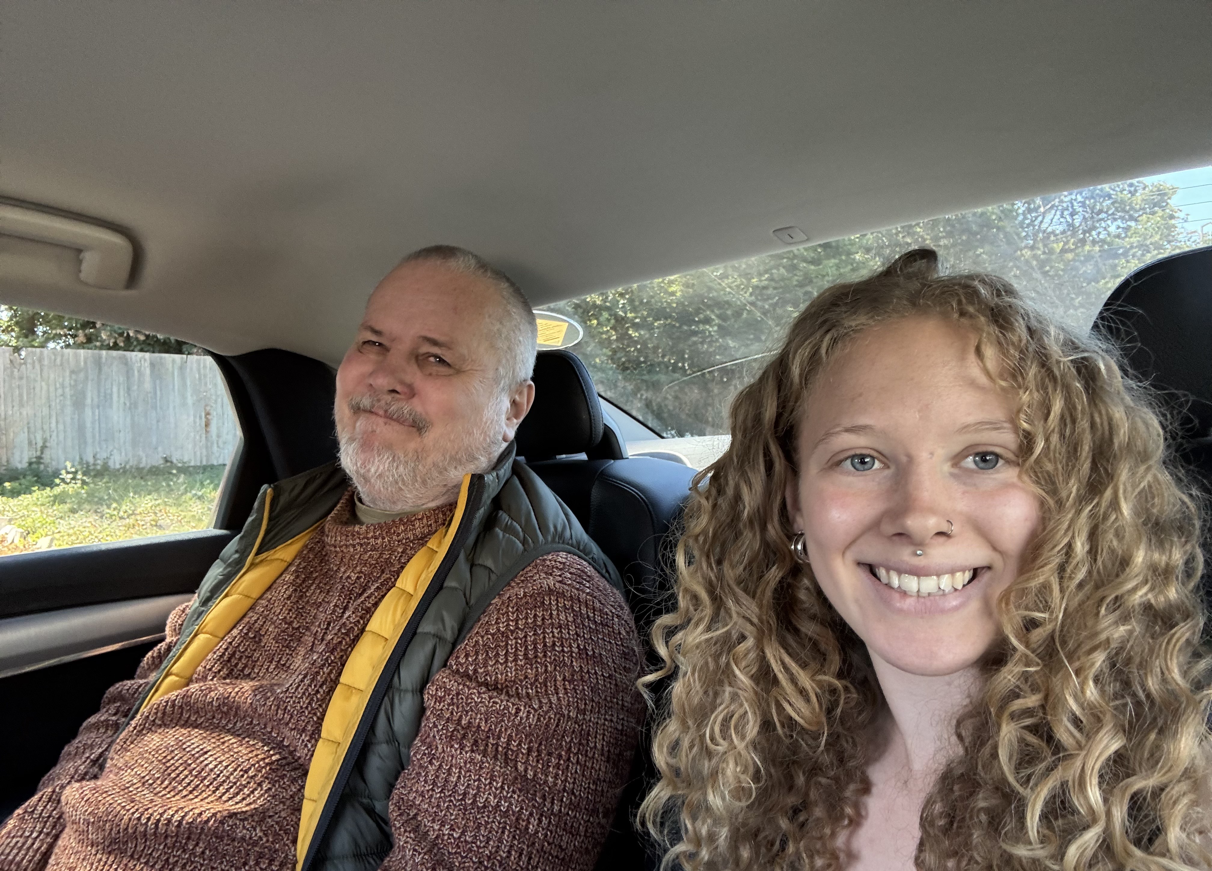 Anna and Mark are sat together in the back seat of a car. They are both smiling at the camera.
