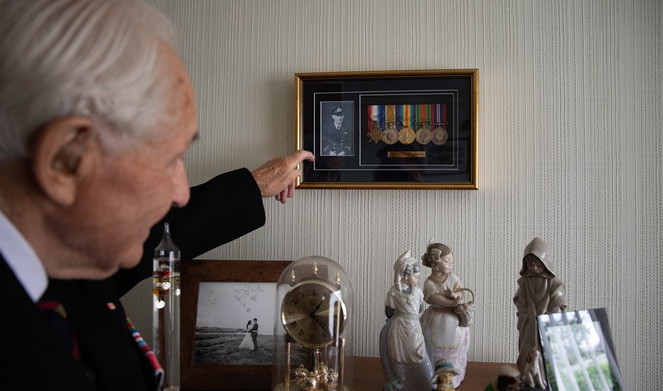 Blind veteran Ron pointing at his framed medals on the wall in his home