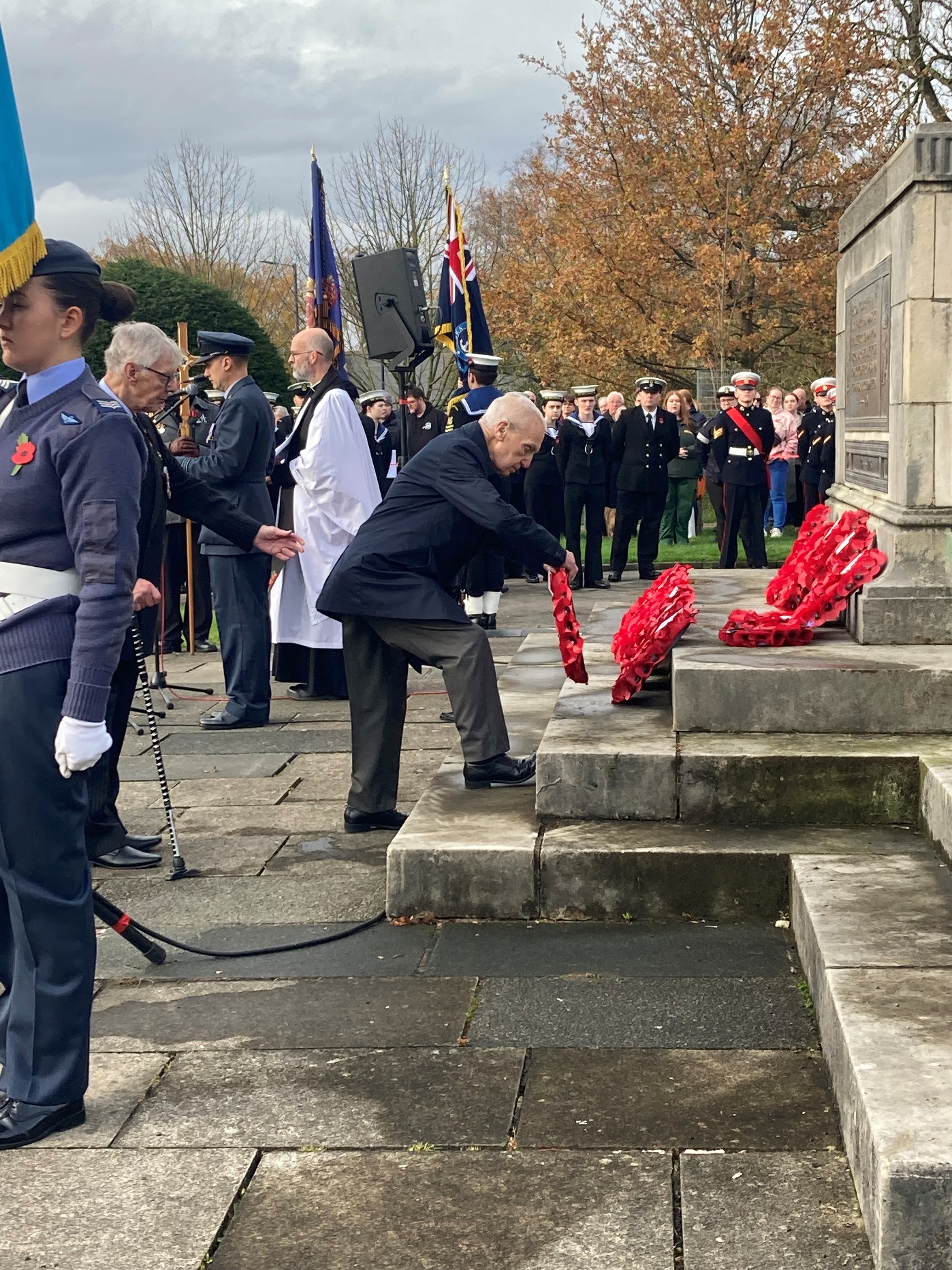 Ken has one foot on the bottom step of the war memorial as he places his wreath