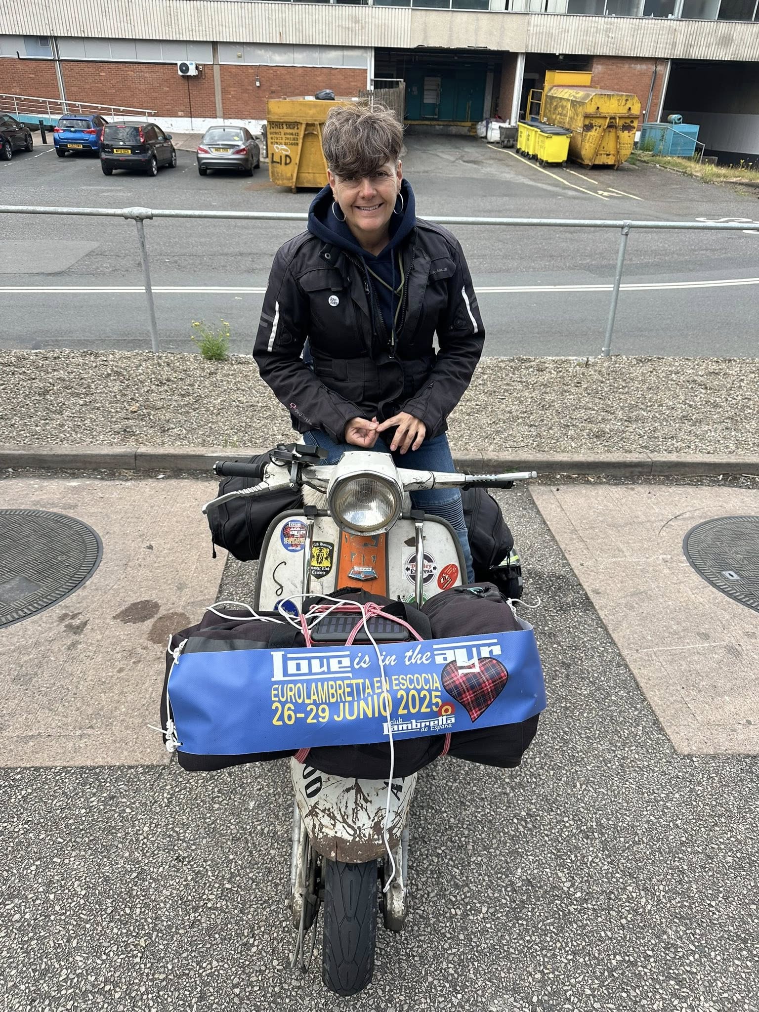 Julie in biker jacket sits on the scooter as it's parked up