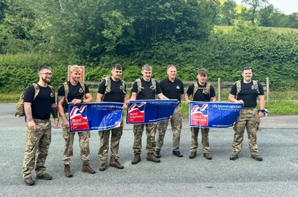 The team of seven walkers wearing camouflage trousers and holding three Blind Veterans UK banners