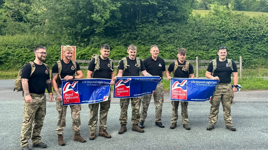 The team of seven walkers wearing camouflage trousers and holding three Blind Veterans UK banners