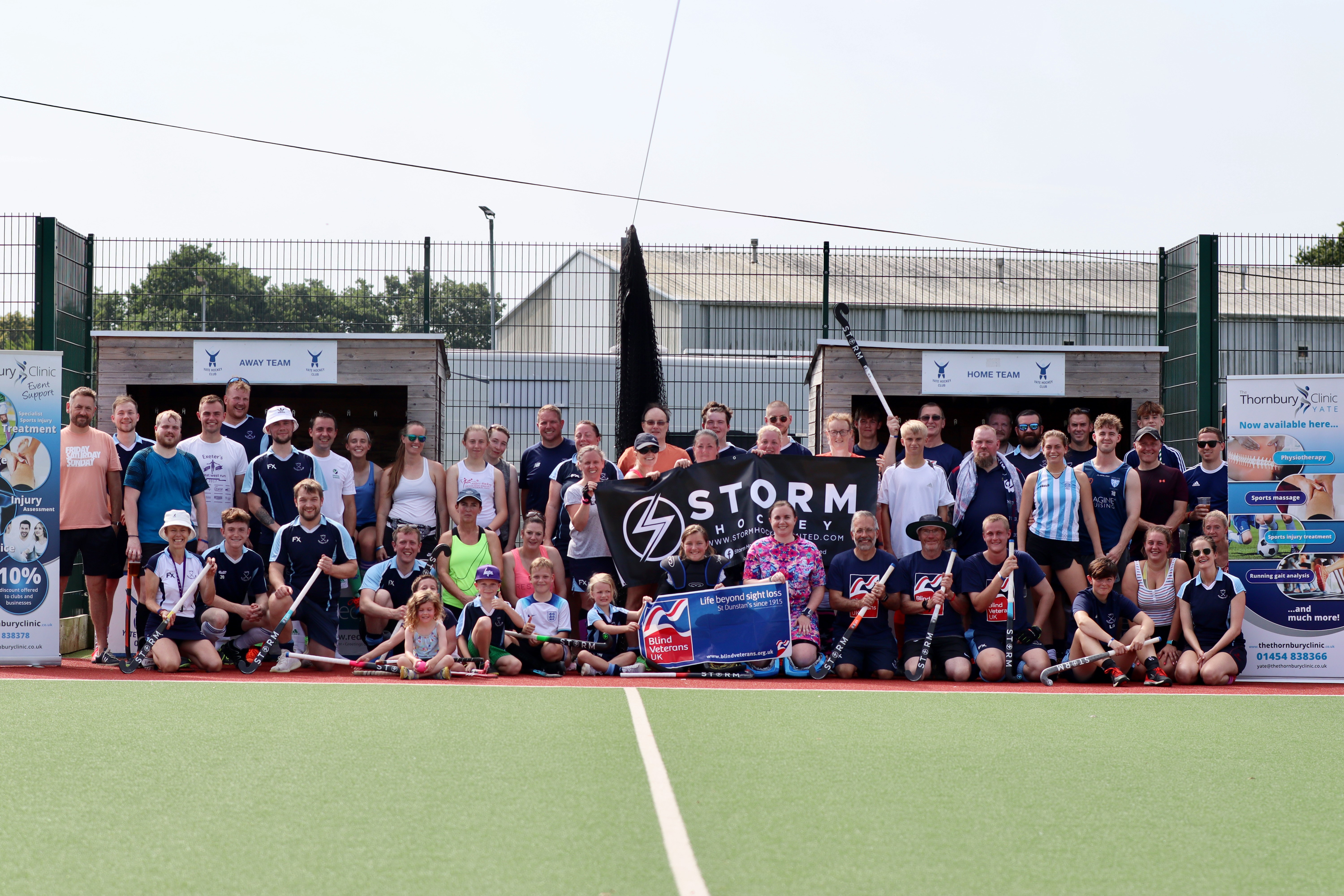 Participants from Yate Hockey Club's President's Day sat at the side of the pitch holding their hockey sticks and a Blind Veterans UK banner
