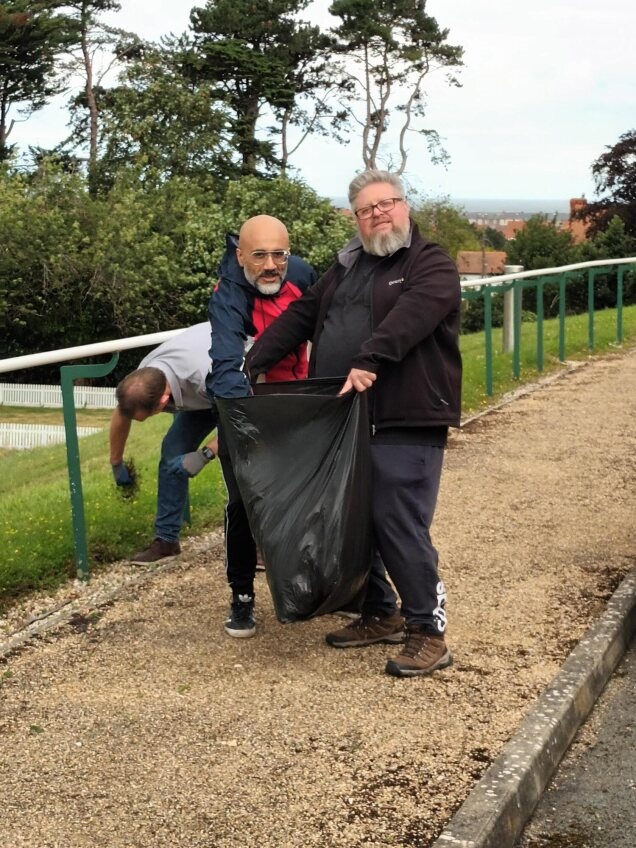 Mark holding open a black bin bag while colleagues place weeds inside