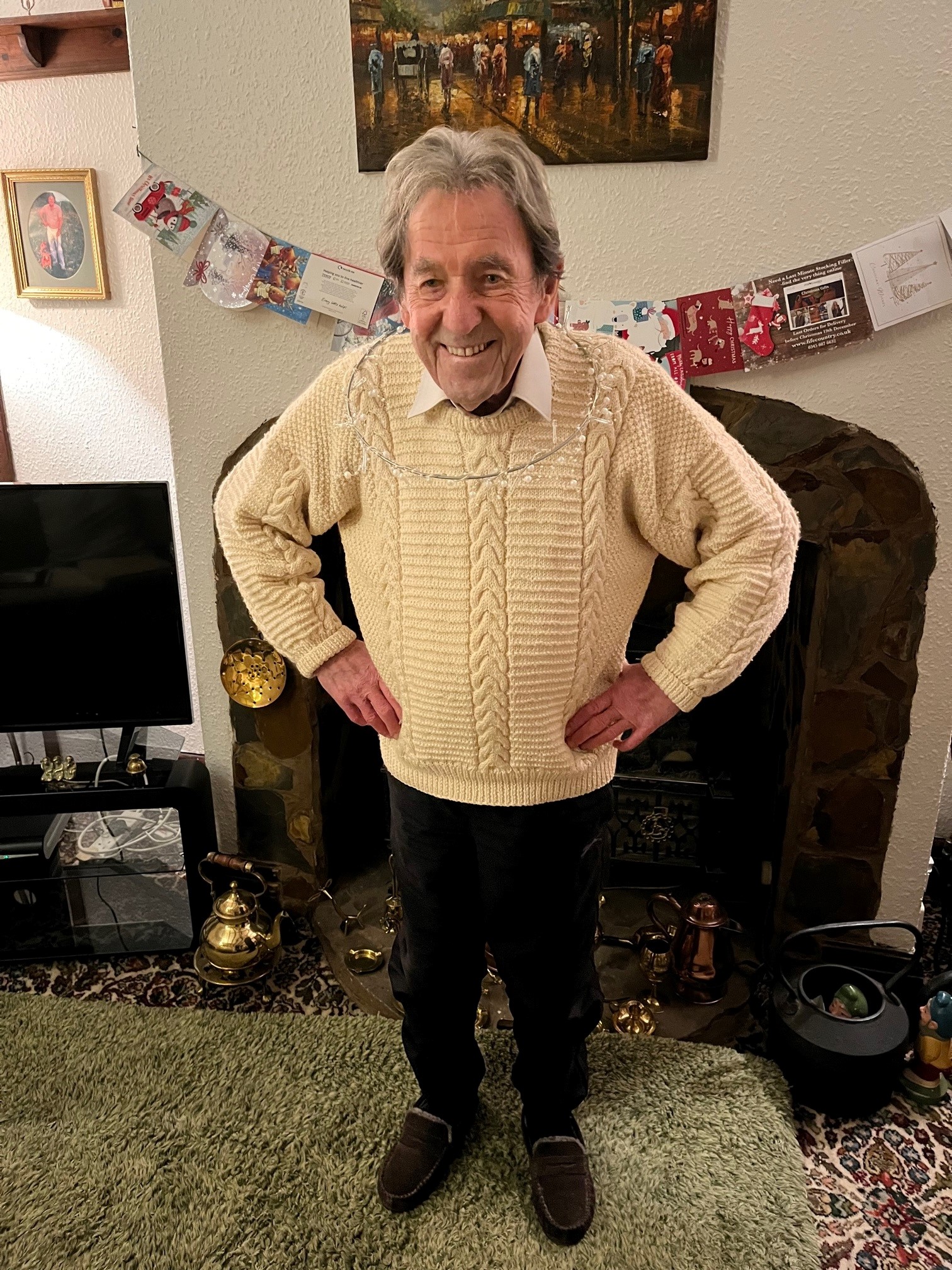 Blind veteran Elwyn stands in front of the fire place, with a Christmas decoration around his neck