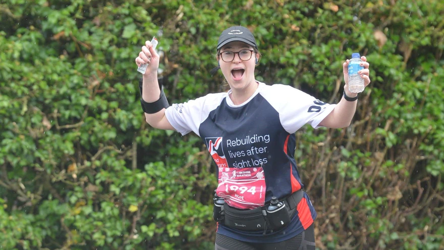 Hope pictured running outside waving her arms in the air, wearing a Blind Veterans UK training top