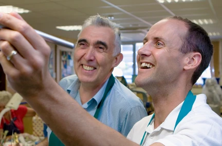 A smiling blind veteran, painting with support from a member of staff