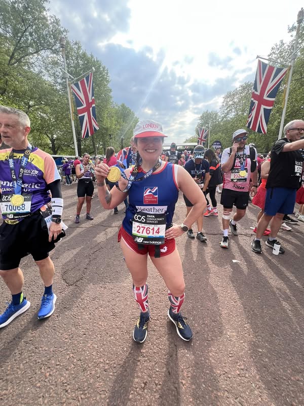 Heather in her Blind Veterans UK running gear and Union Flag socks, stood proudly at the bottom of Pall Mall, surrounded by crowds , smiling at the camera as she holds up her London Marathon medal.