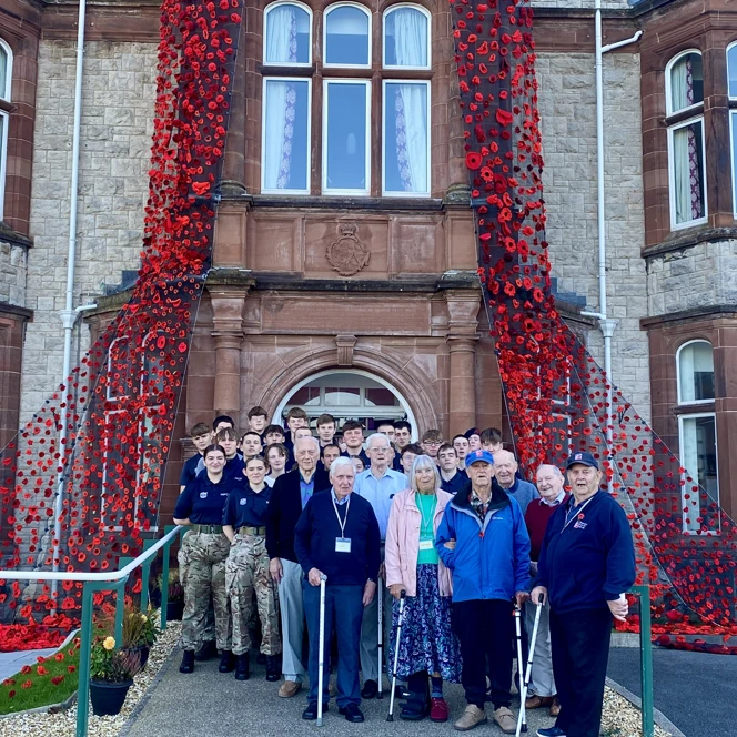 A group of veterans and volunteers stand outside the entrance of our Llandudno Centre, which is decorated with the cascading poppy blanket