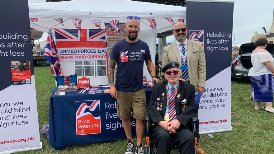 A Blind Veterans UK display stand set up with leaflets and posters with members of staff and blind veteran David stood in front