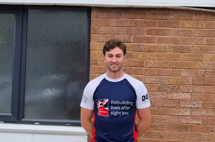James stood wearing his Blind Veterans UK t shirt in front of a sign for Gwynedd Forklifts