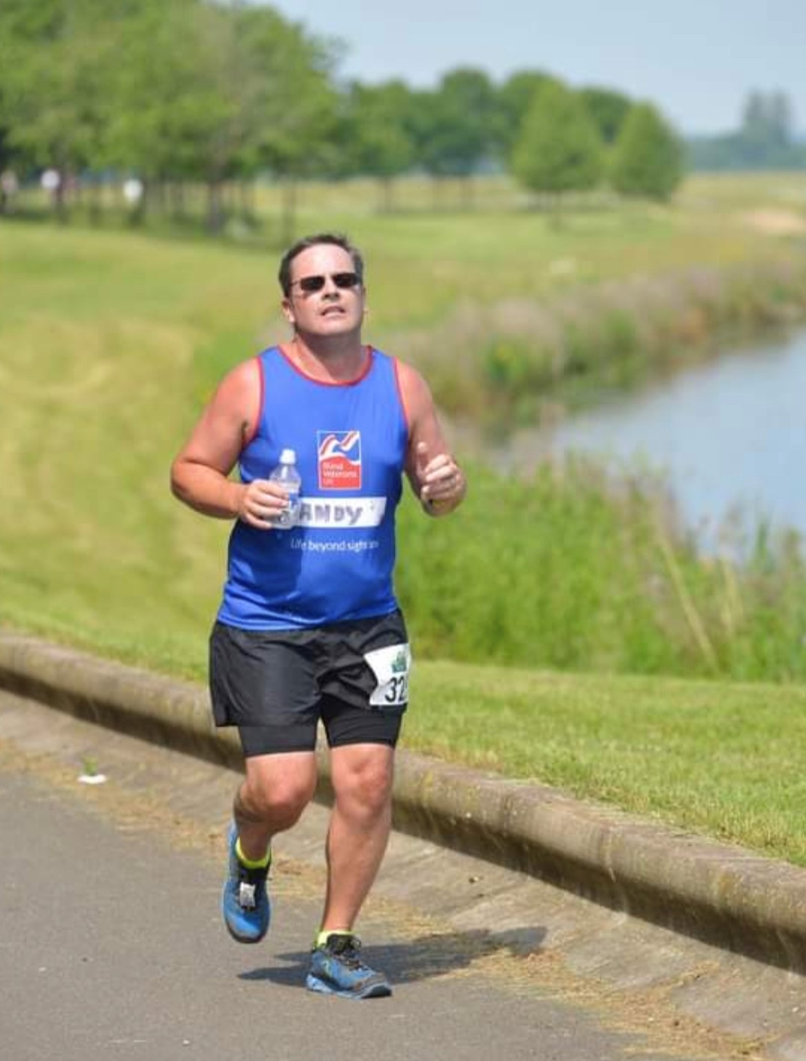 Andy is running top and shorts running on a path alongside a pond