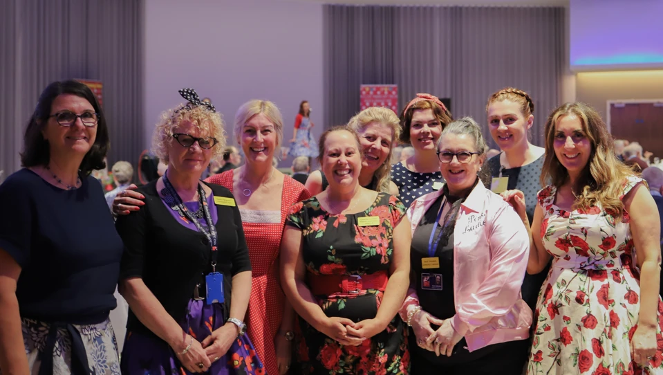 A group of nine Blind Veteran UK staff members at an event, gathered together and smiling