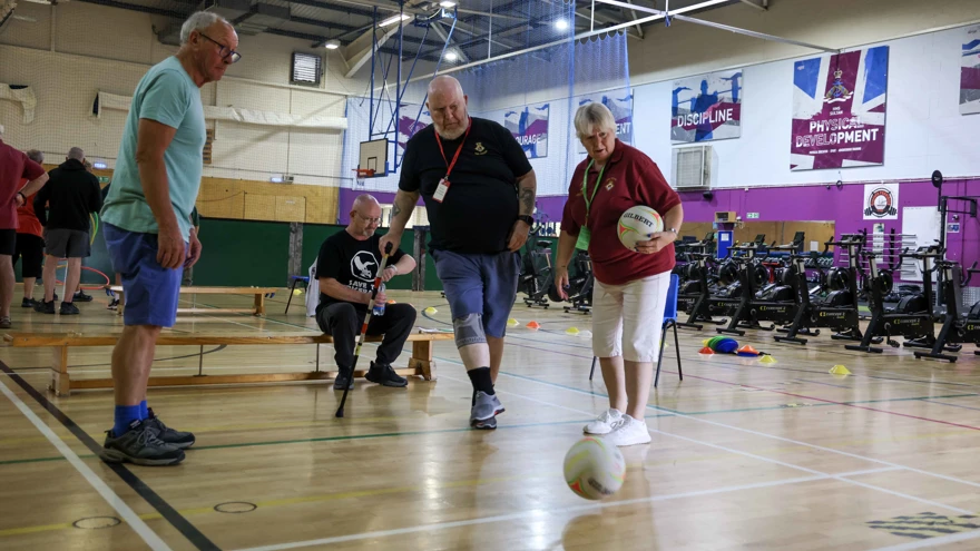 A blind veteran kicks a football, supported by two guides
