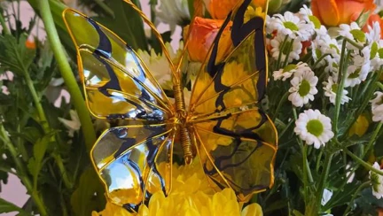 A vibrant resin butterfly with yellow and black waves of colour in a vase of flowers