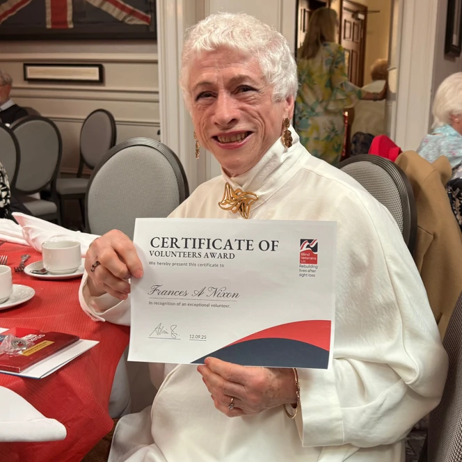 Frances is seated at a table and smiling as she holds her certificate.