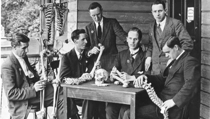 A group of vision-impaired veterans study anatomy using a skeleton model and bone replicas during a massage training session.