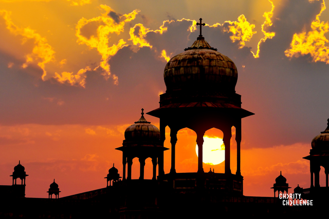 Silhouettes of the city's turrets against a pink sunset sky, with grey-purple clouds with golden edges where the sun's rays are lighting them up. 