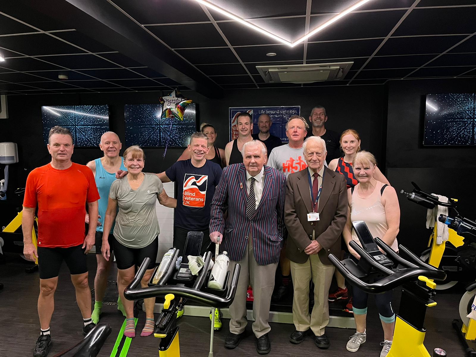 A group shot of all those who took part in the challenge stood behind two spin bikes