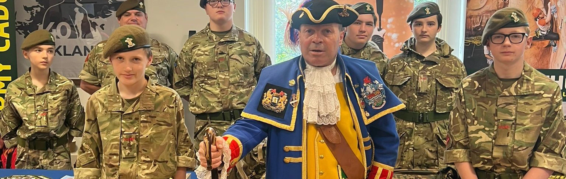 Billy in his town crier coat stood with uniformed Army Cadets at a table laid out with information about their organisation