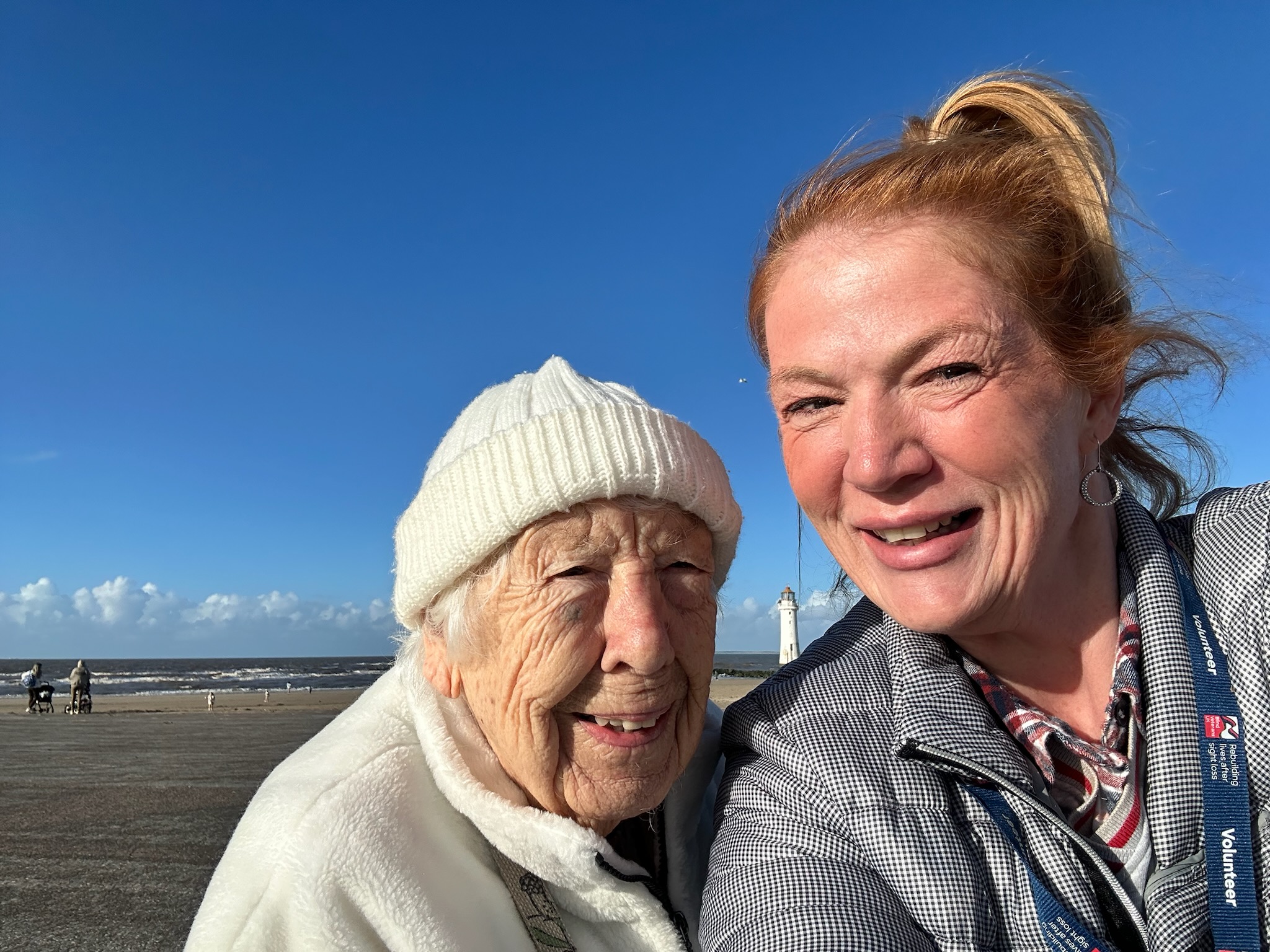 Olly and Lanie smiling at the seafront in New Brighton. A lighthouse can be seen in the background.