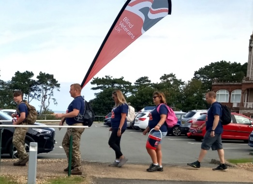 A group of five from the Wrexham Army Careers Office walking in a line with one carrying a large Blind Veterans UK flag
