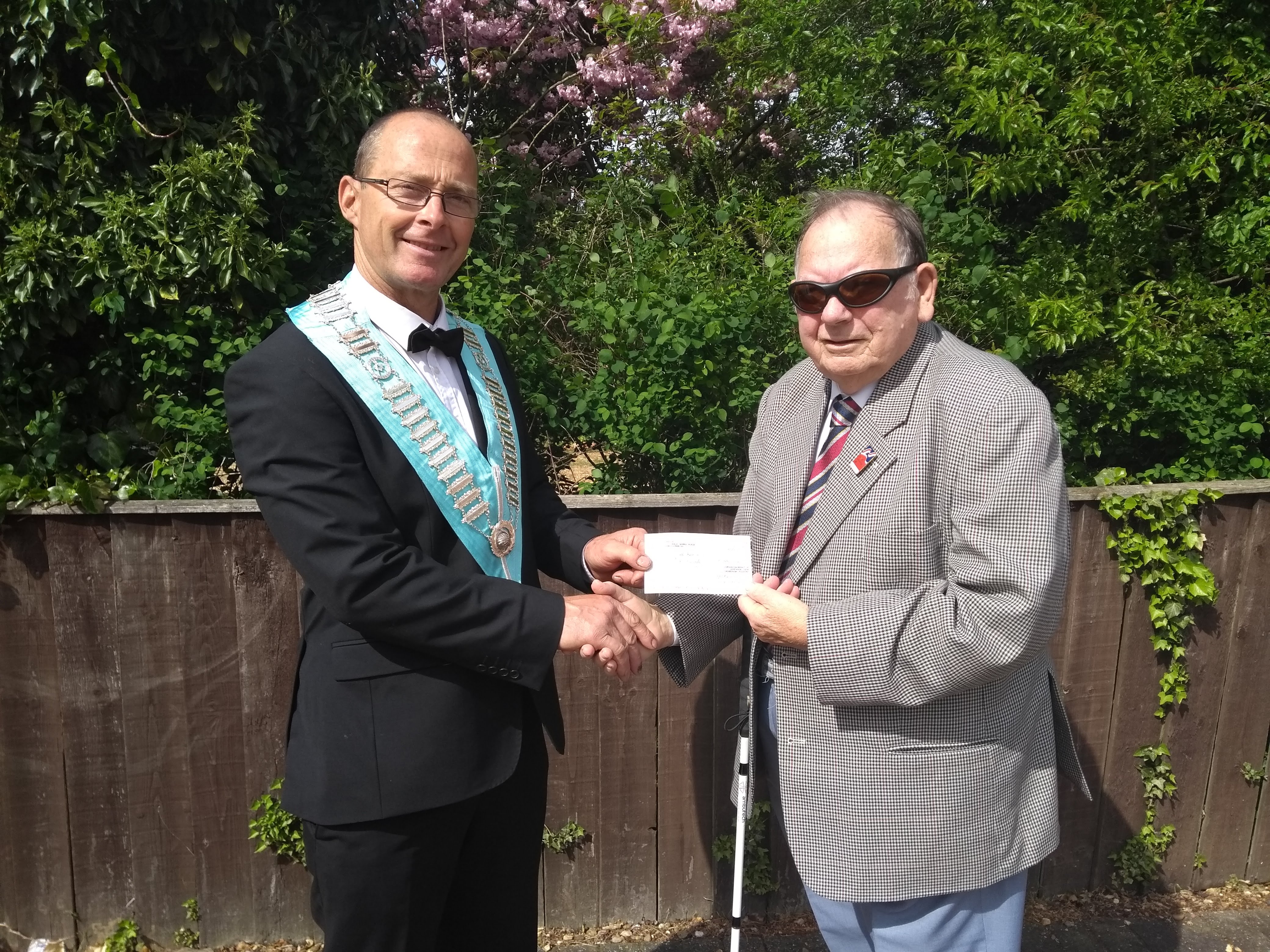 A blind veteran and a man shaking hands and holding up a cheque