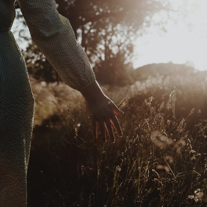A photo of a person walking through grass during sunrise