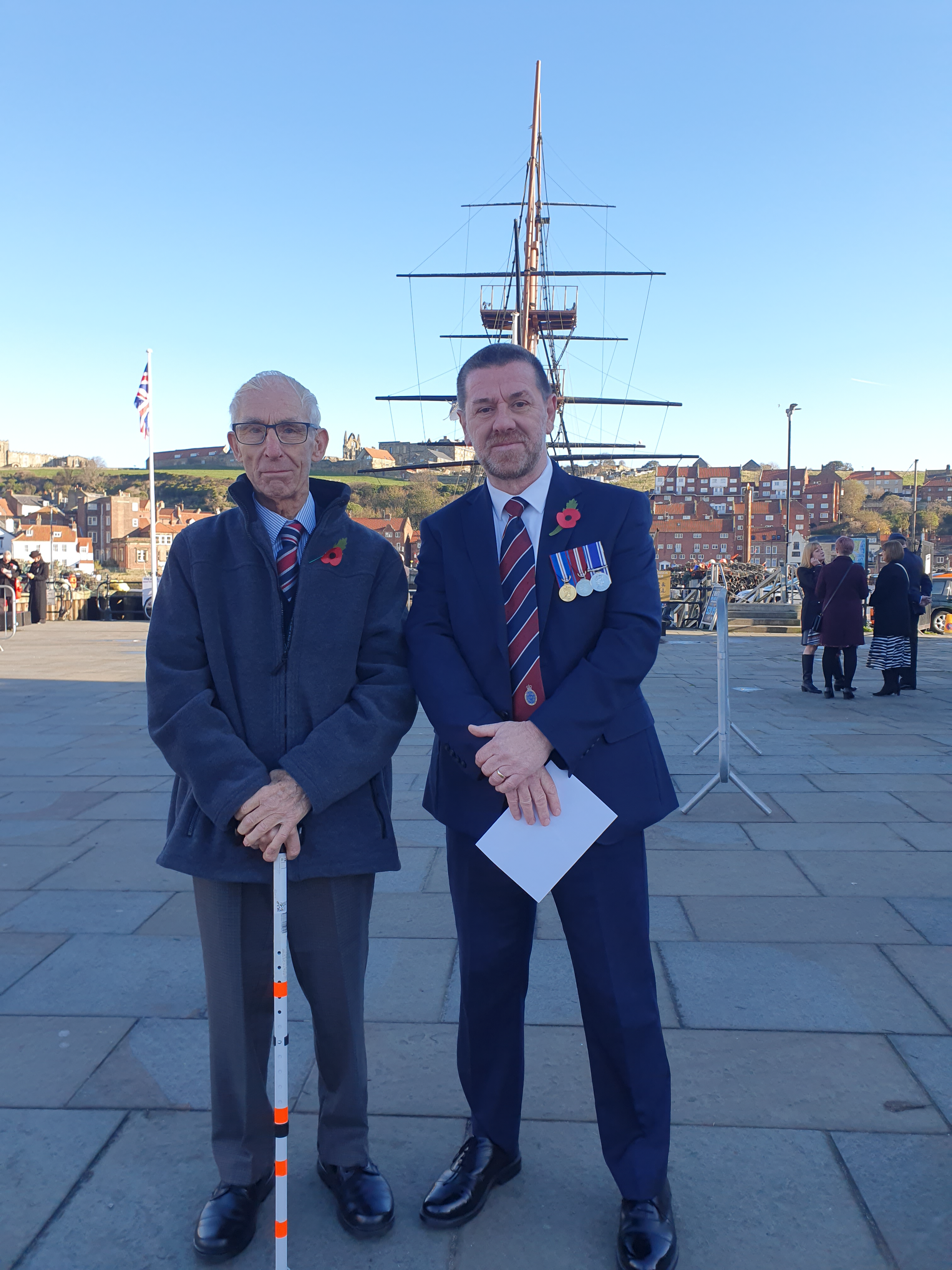 Blind veterans Alan and Andy at Whitby Remembrance service standing in front of a ship