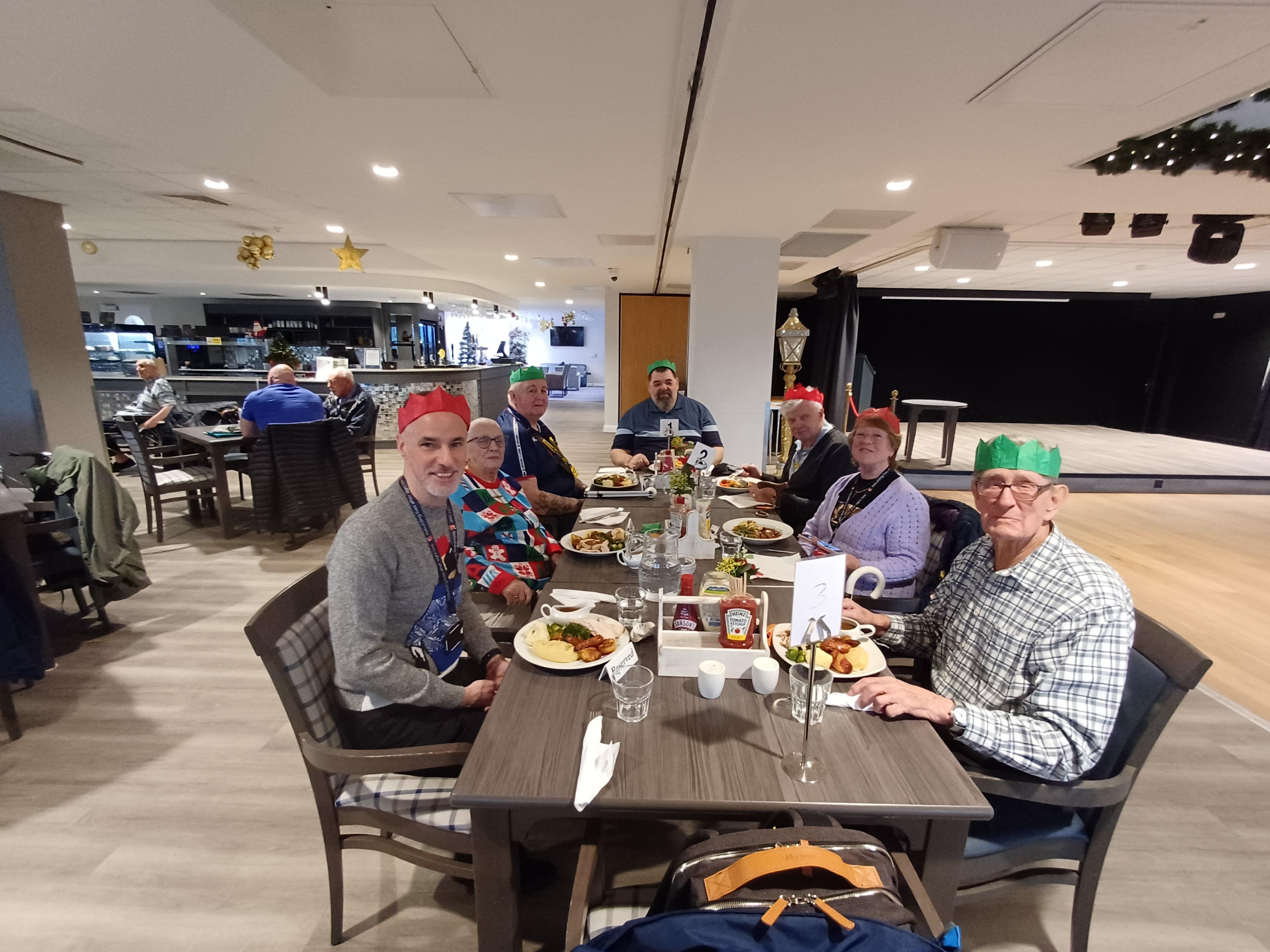 The veterans and staff sit around a table wearing Christmas hats and look into camera