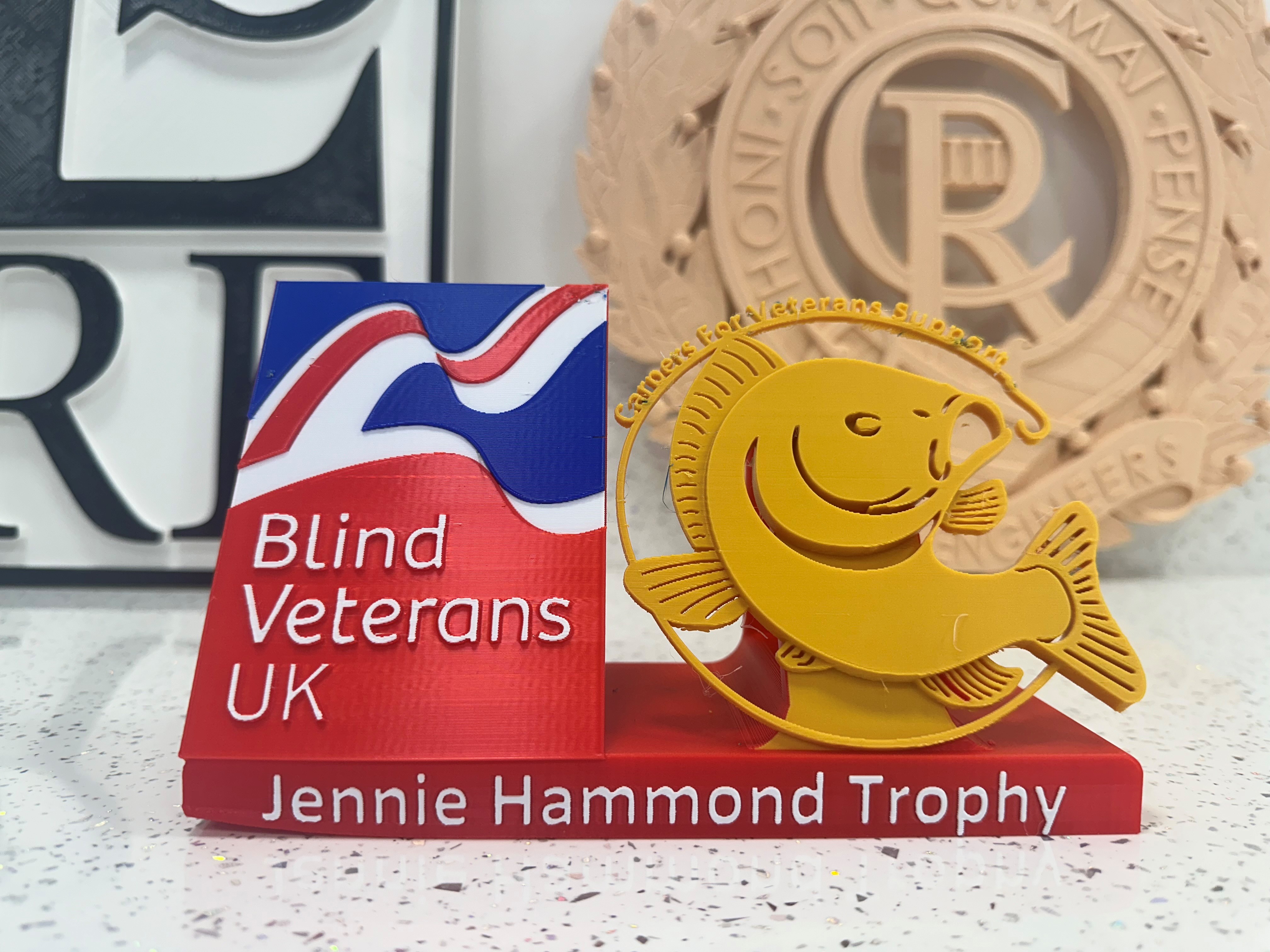 Blind Veterans UK logo on the left, beside a gold silhouette of a carp with text above 'Carpers for Veterans Support' on the right, and text below 'Jennie Hammond Trophy'