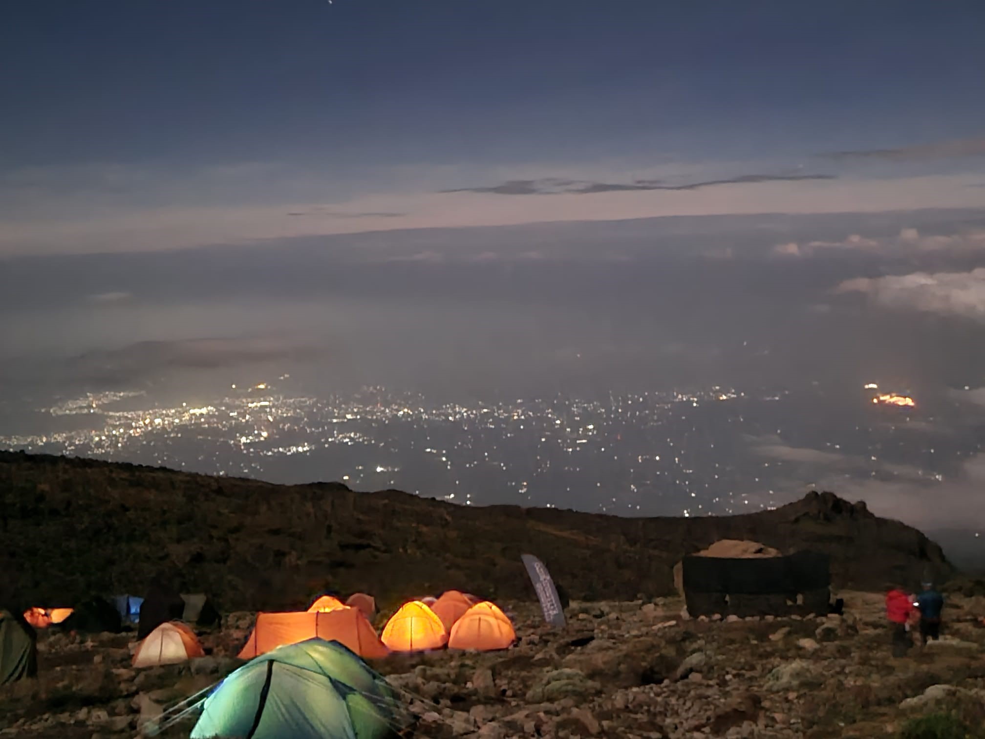 A selection of tents all glowing due to torch lights inside, high on the side of the mountain